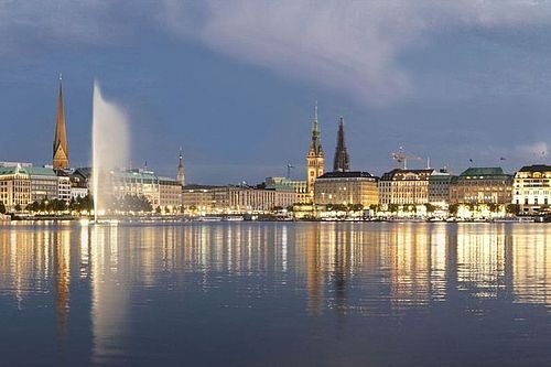 Sicht von der Alster zum Jungfernstieg bei Nacht. Die Lichter spiegeln sich im Wasser.