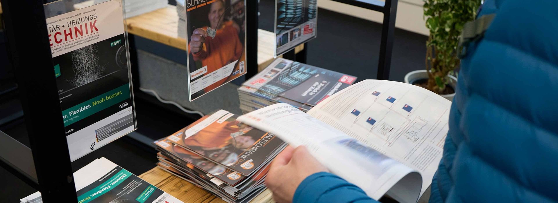 Blick von schräg oben auf einen Mann, der in einer Zeitschrift in der Medien Lounge blättert. Vor ihm steht ein Regal mit weiteren Zeitschriften.