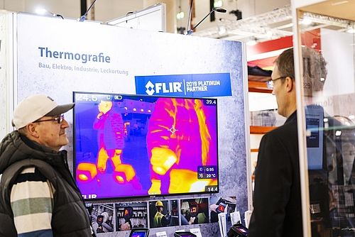 Aussteller und Besucher betrachten thermographische Aufnahmen auf einem Bildschrim