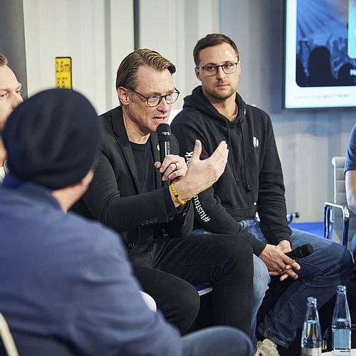 Fünf Menschen sitzen in der Runde, wahrend einer davon ins Mikrofon spricht. 