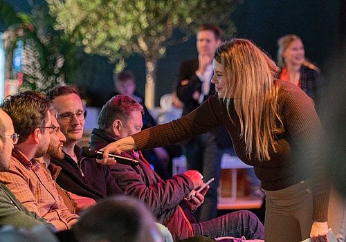 Situation in der GET NORD Arena: Die Moderatorin streckt einem Teilnehmer im Publikum das Mikrophon entgegen, damit dieser sich aktiv am Programm beteiligen kann.