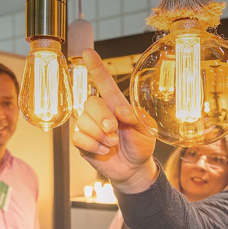 Nahaufnahme einer Ausstellung von Glühbirnen, Aussteller und Besucher im Hintergrund