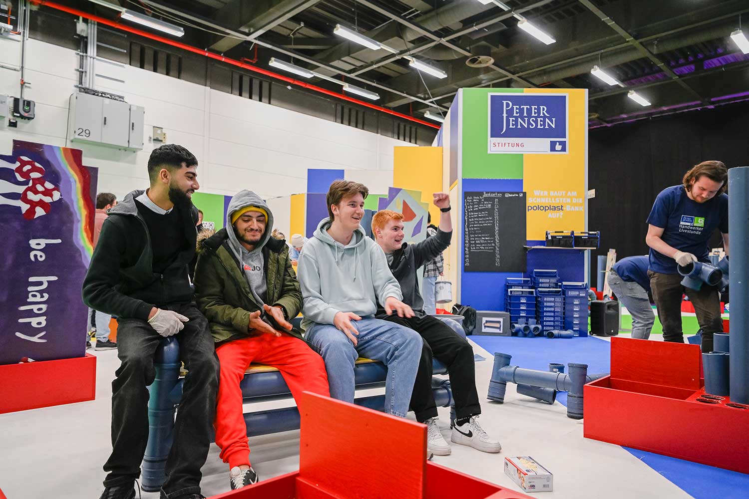 Vier junge Männer sitzen gut gelaunt auf einigen Rohren an einem Stand auf der GET NORD.